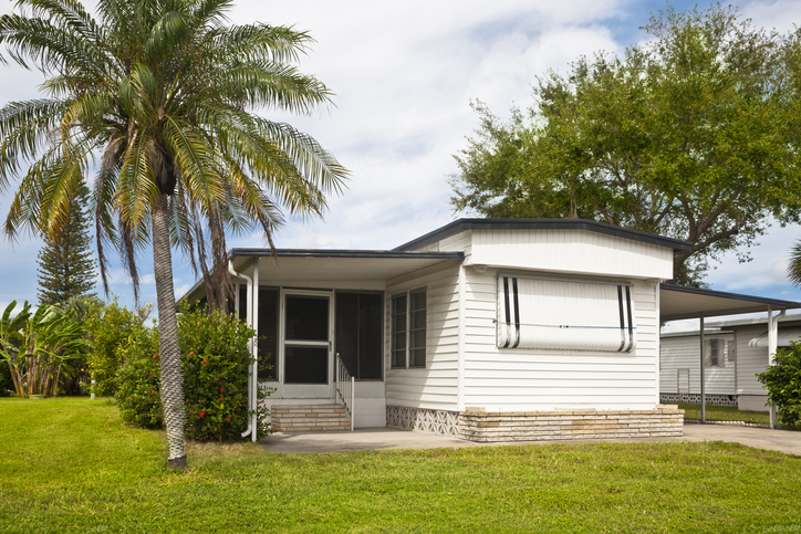 Mobile home with palm tree and front lawn. A static caravan holiday home, a vacation home or retirement home located in a trailer park.