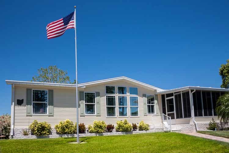 Mobile home with American flag, front lawn and clear blue sky. buying a mobile home.