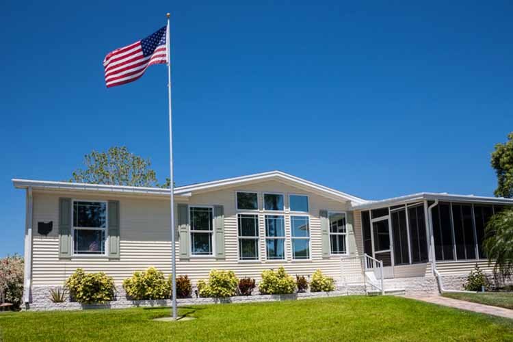 Mobile home with American flag, front lawn and clear blue sky.